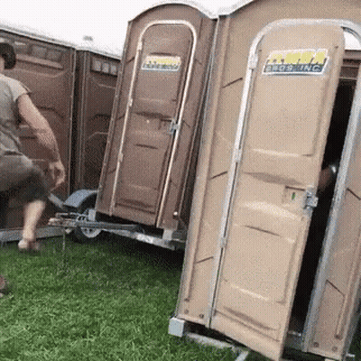 A Man Is Standing Next To A Trailer With Portable Toilets Attached To It And One Of Them Is Open GIF
