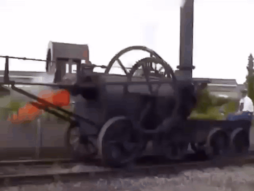 A Man Is Standing Next To A Train That Is On The Tracks . GIF