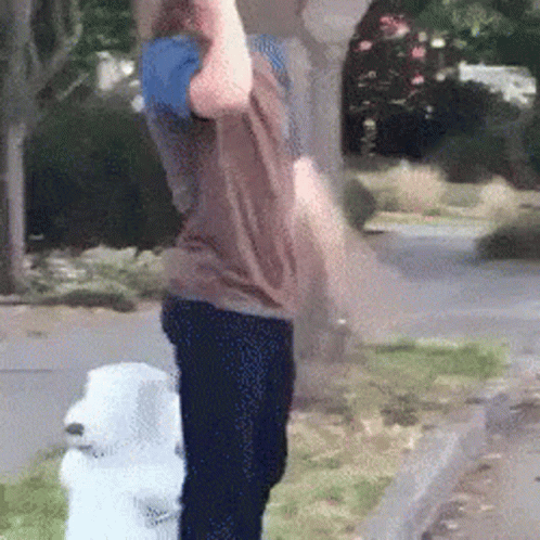 A Man Is Standing Next To A White Dog On The Sidewalk . GIF