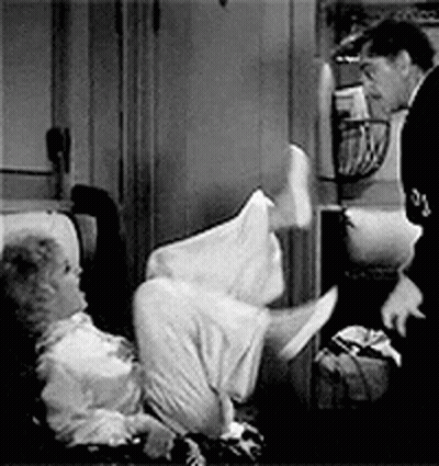 A Man Is Standing Next To A Woman Laying On A Couch . GIF