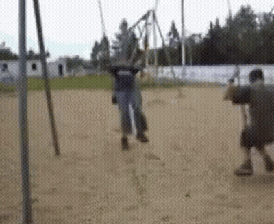 A Man Is Standing Next To A Woman On A Swing In A Playground . GIF