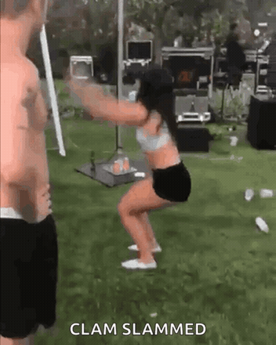 A Man Is Standing Next To A Woman Squatting In The Grass . GIF