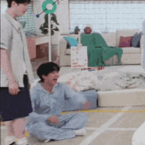 A Man Is Standing Next To A Woman Who Is Sitting On The Floor In A Living Room . GIF