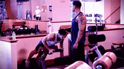 A Man Is Standing Next To Another Man In A Gym Doing Exercises . GIF
