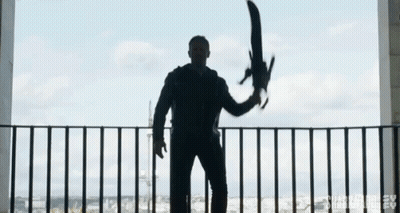 A Man Is Standing On A Balcony Holding A Large Sword In His Hand . GIF