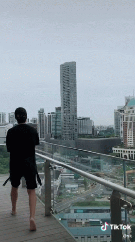 A Man Is Standing On A Balcony Looking At A City Skyline GIF