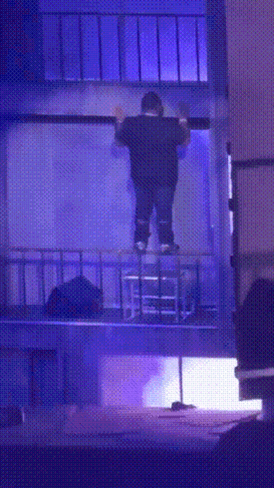 A Man Is Standing On A Balcony With A Blue Light Behind Him GIF