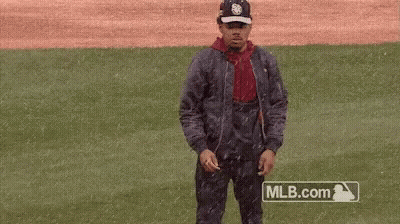 A Man Is Standing On A Baseball Field Wearing A Jacket And Hat . GIF