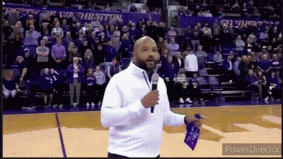 A Man Is Standing On A Basketball Court Holding A Microphone In Front Of A Crowd Of People . GIF