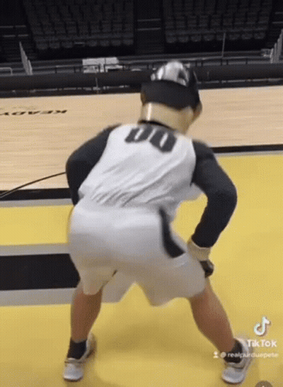 A Man Is Standing On A Basketball Court Wearing A Baseball Uniform And A Hat . GIF