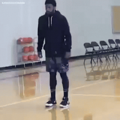 A Man Is Standing On A Basketball Court Wearing A Black Hoodie And Shorts . GIF