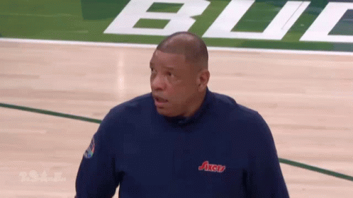 A Man Is Standing On A Basketball Court Wearing A Blue Axcu Shirt GIF