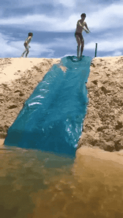 A Man Is Standing On A Blue Tarp That Is Going Into The Water GIF