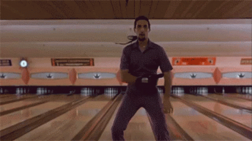 A Man Is Standing On A Bowling Alley Holding A Bowling Ball In His Hand GIF