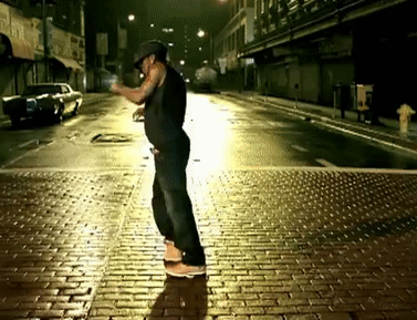 A Man Is Standing On A Brick Sidewalk At Night With A Fire Hydrant In The Background GIF