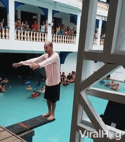A Man Is Standing On A Diving Board In Front Of A Crowd Of People . GIF