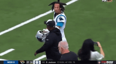 A Man Is Standing On A Football Field Talking To A Player . GIF
