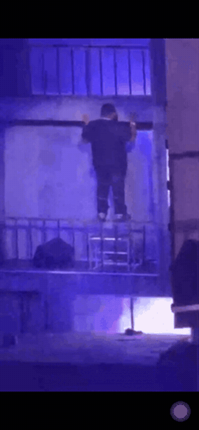 A Man Is Standing On A Ladder In A Dark Room With Blue Lights Behind Him . GIF