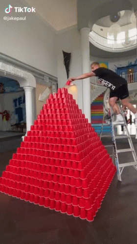 A Man Is Standing On A Ladder In Front Of A Pyramid Made Of Red Cups GIF