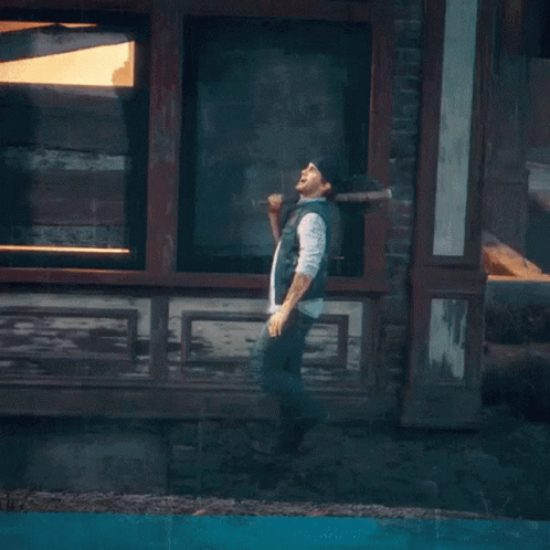 A Man Is Standing On A Lamp Post In Front Of A Brick Wall With Graffiti On It That Says Riot GIF
