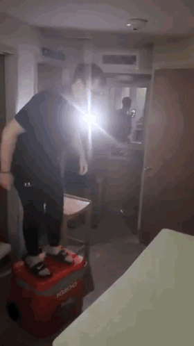 A Man Is Standing On A Red Cooler In A Room . GIF