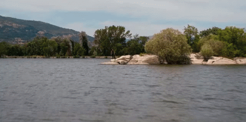 A Man Is Standing On A Rock In The Middle Of A Lake GIF