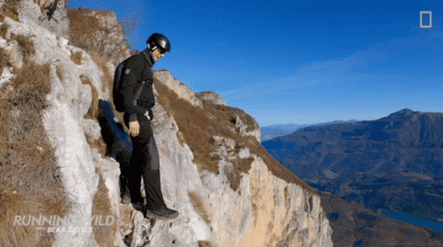 A Man Is Standing On A Rocky Cliff With The Words Running Wild Bear Grylls On The Bottom GIF