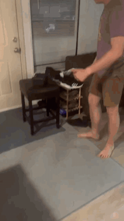 A Man Is Standing On A Rug In A Living Room Holding A Pair Of Shoes GIF