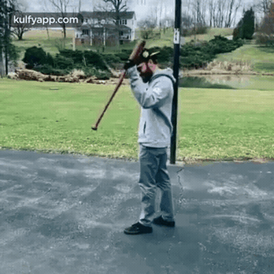 A Man Is Standing On A Sidewalk Holding A Cane And A Bat . GIF