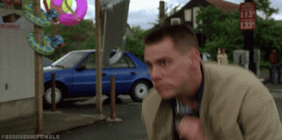 A Man Is Standing On A Sidewalk In Front Of A Blue Car And Talking On A Cell Phone . GIF