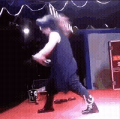 A Man Is Standing On A Stage Holding A Microphone And A Guitar . GIF