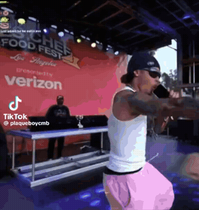A Man Is Standing On A Stage Holding A Microphone In Front Of A Sign That Says Verizon . GIF