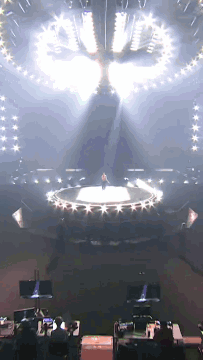 A Man Is Standing On A Stage With A Circle Of Lights Around Him GIF