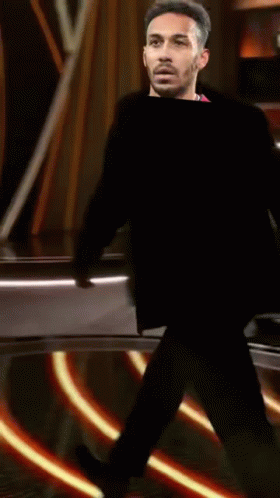 A Man Is Standing On A Stage With A Reflection Of Him In A Mirror . GIF