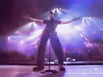 A Man Is Standing On A Stage With His Arms Outstretched . GIF