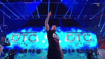A Man Is Standing On A Stage With His Hand In The Air In Front Of A Sign That Says Oto Oto GIF