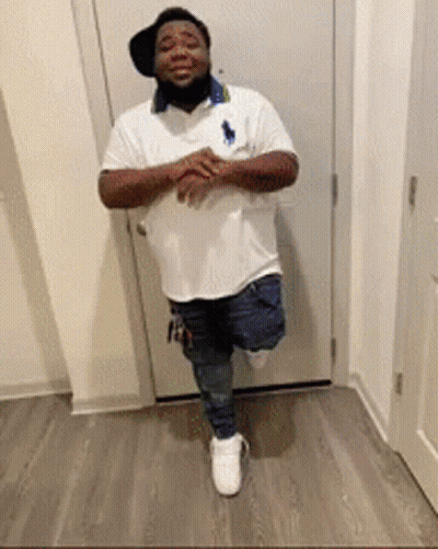 A Man Is Standing On One Leg In Front Of A Door Wearing A Hat And A White Shirt . GIF