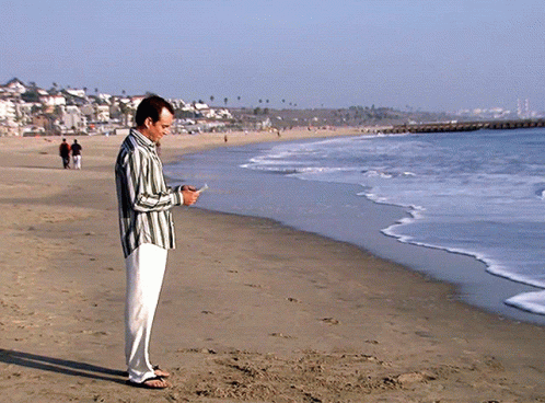A Man Is Standing On The Beach Looking At His Phone GIF