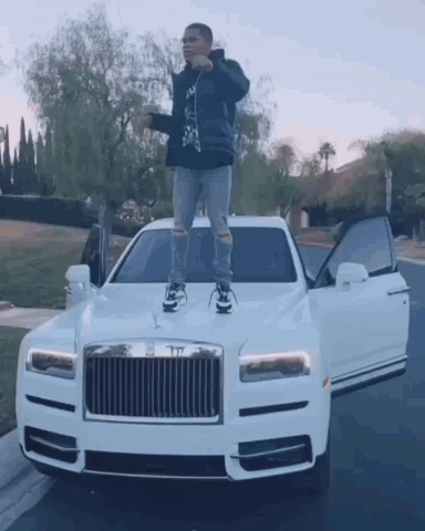 A Man Is Standing On The Hood Of A White Rolls Royce Car . GIF