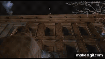A Man Is Standing On The Roof Of A Tall Building At Night . GIF