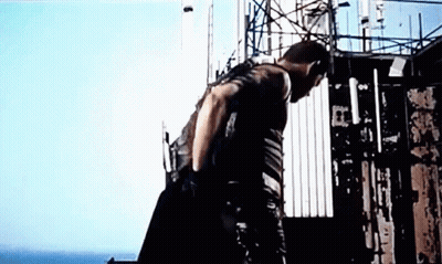 A Man Is Standing On Top Of A Building With A Gun . GIF
