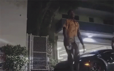 A Man Is Standing On Top Of A Car In Front Of A Building At Night . GIF