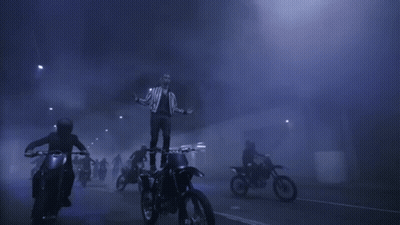A Man Is Standing On Top Of A Dirt Bike In The Middle Of A Crowd Of People Riding Motorcycles . GIF