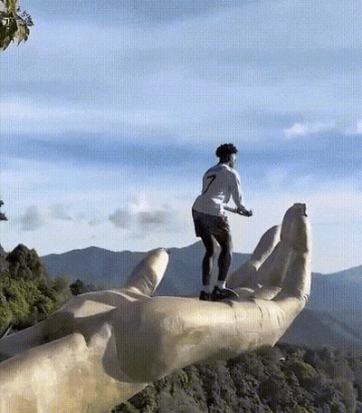 A Man Is Standing On Top Of A Giant Hand With Mountains In The Background GIF