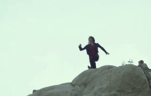 A Man Is Standing On Top Of A Large Rock . GIF