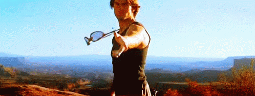 A Man Is Standing On Top Of A Mountain Holding A Pair Of Sunglasses In His Hand . GIF
