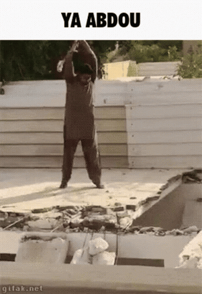 A Man Is Standing On Top Of A Pile Of Concrete With The Words Ya Abdou Written Above Him . GIF