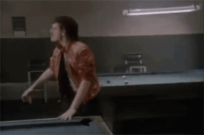 A Man Is Standing On Top Of A Pool Table In A Pool Hall . GIF