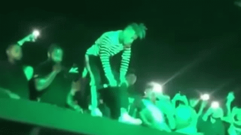 A Man Is Standing On Top Of A Stage In Front Of A Crowd Of People . GIF