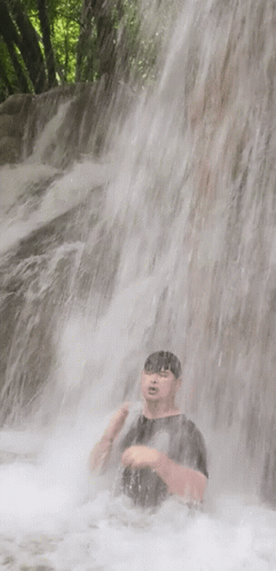 A Man Is Standing Under A Waterfall With His Head In The Water GIF